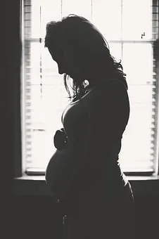 A pregnant woman standing in front of a window.