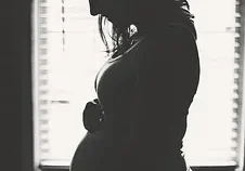 A pregnant woman standing in front of a window.