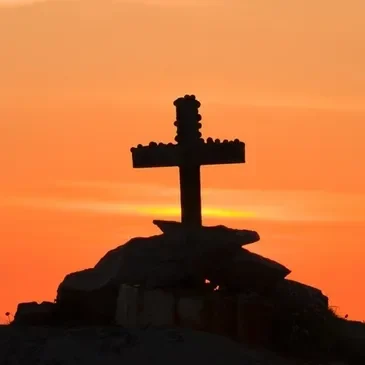 A cross on top of a hill at sunset.